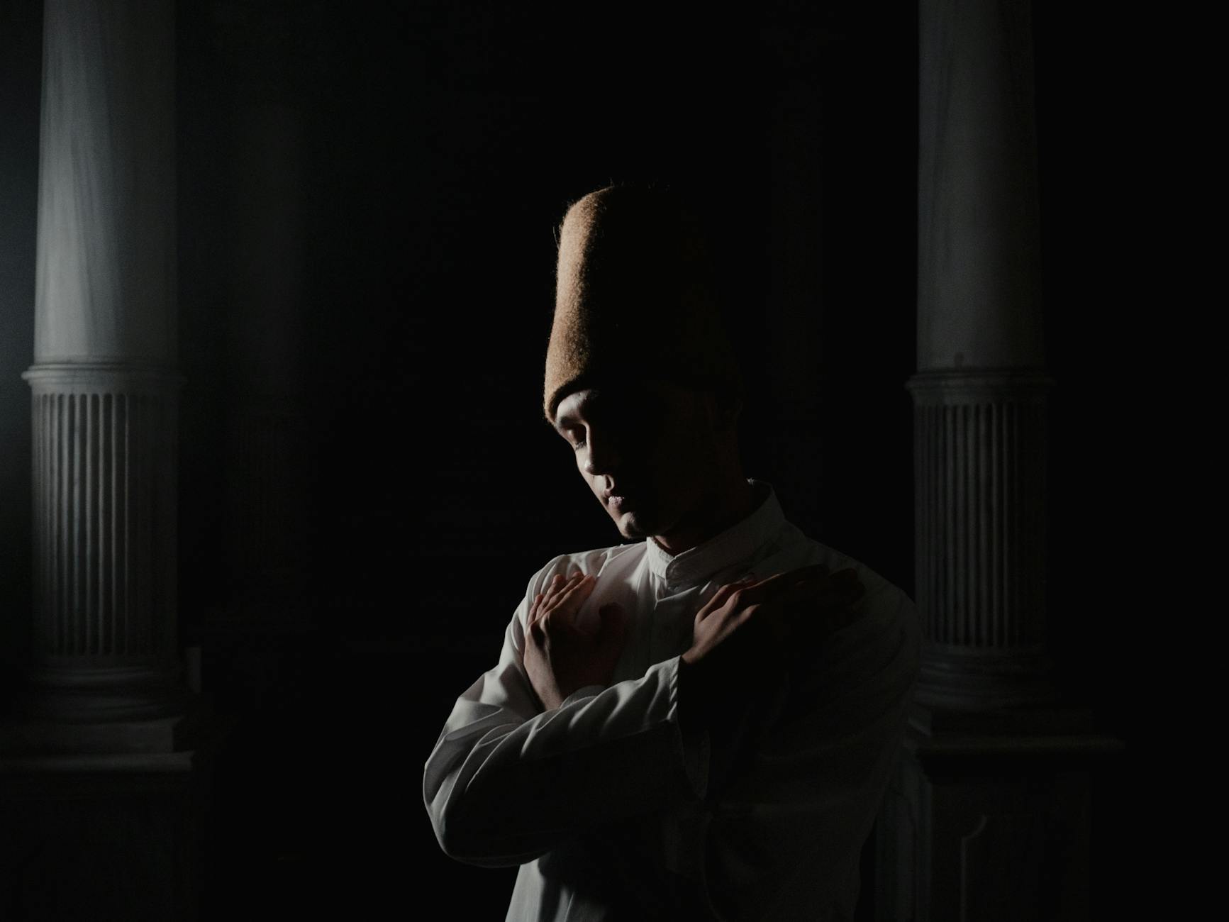 Ein Derwisch mit traditioneller Sikke-Kopfbedeckung hält die Hände zur Meditation gekreuzt.