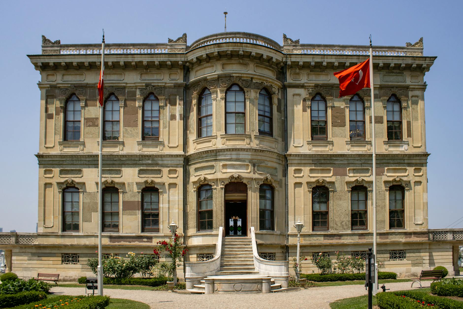 Frontalansicht des Küçüksu-Kasrı mit wehenden türkischen Flaggen unter blauem Himmel.