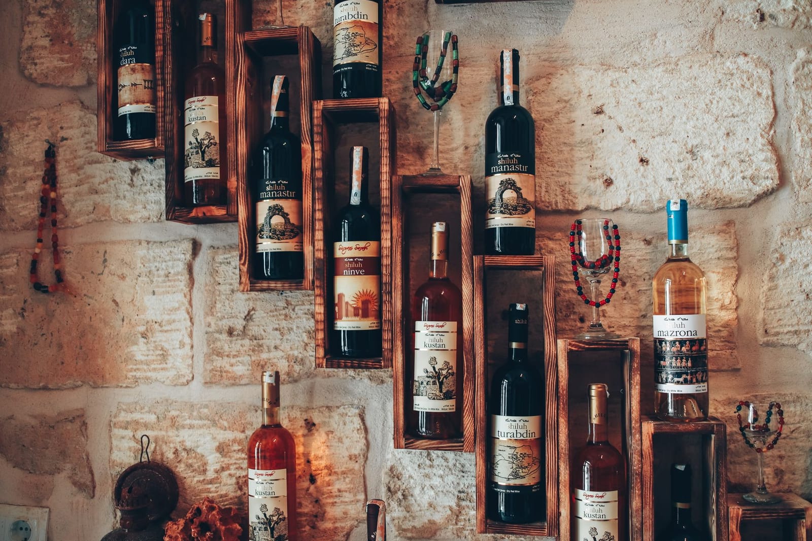 Flaschen lokaler Rebsorten lagern in Holzkästen an einer rustikalen Steinwand.