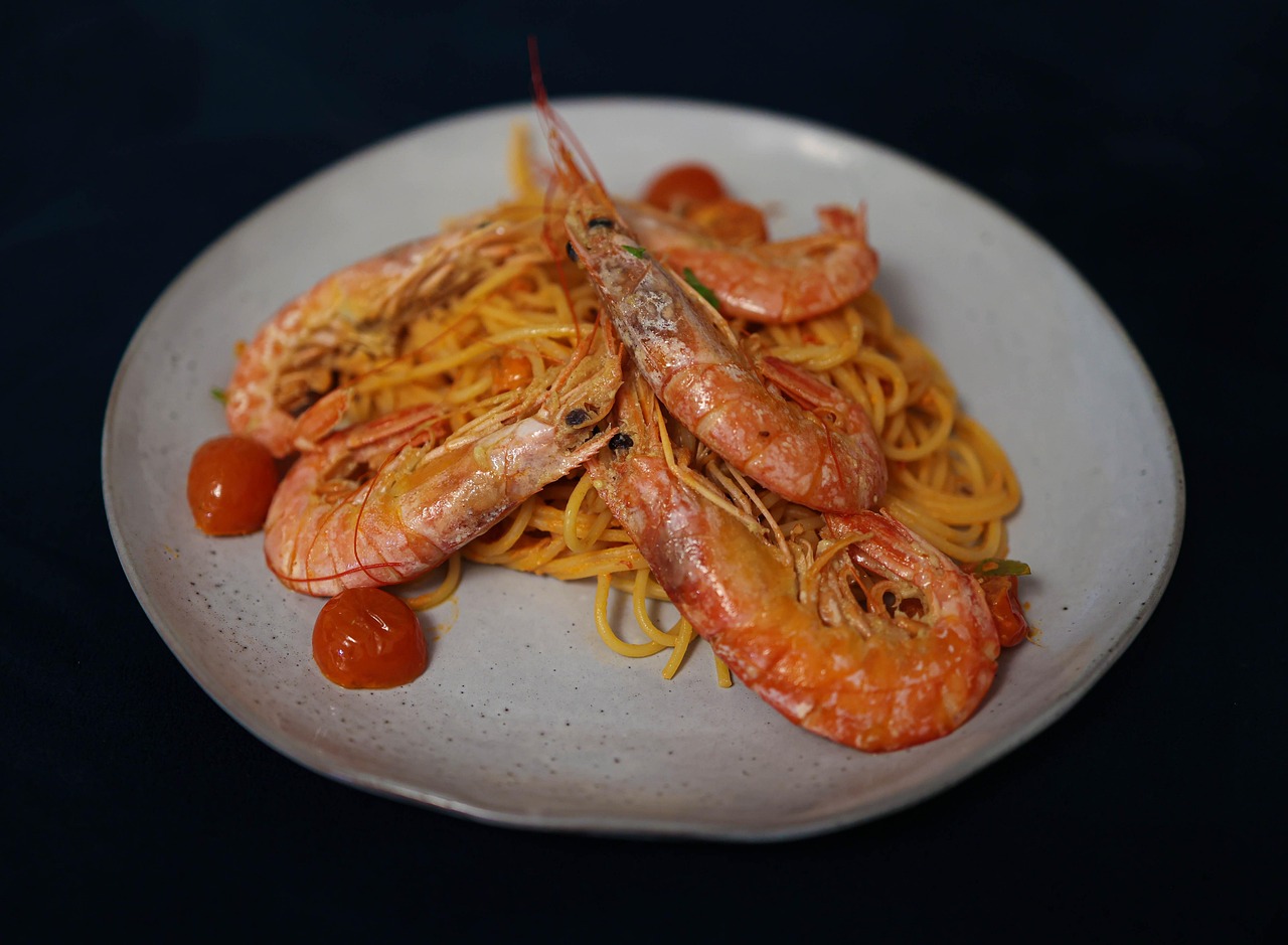 Spaghetti mit großen gebratenen Garnelen und Kirschtomaten auf einem hellen Keramikteller.