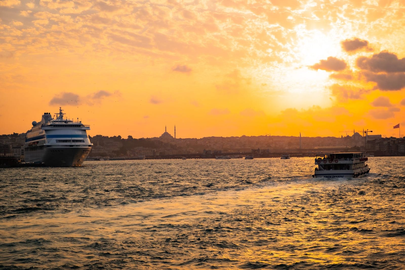 Ein Ausflugsboot auf dem Bosporus vor der Silhouette Istanbuls im Abendlicht.