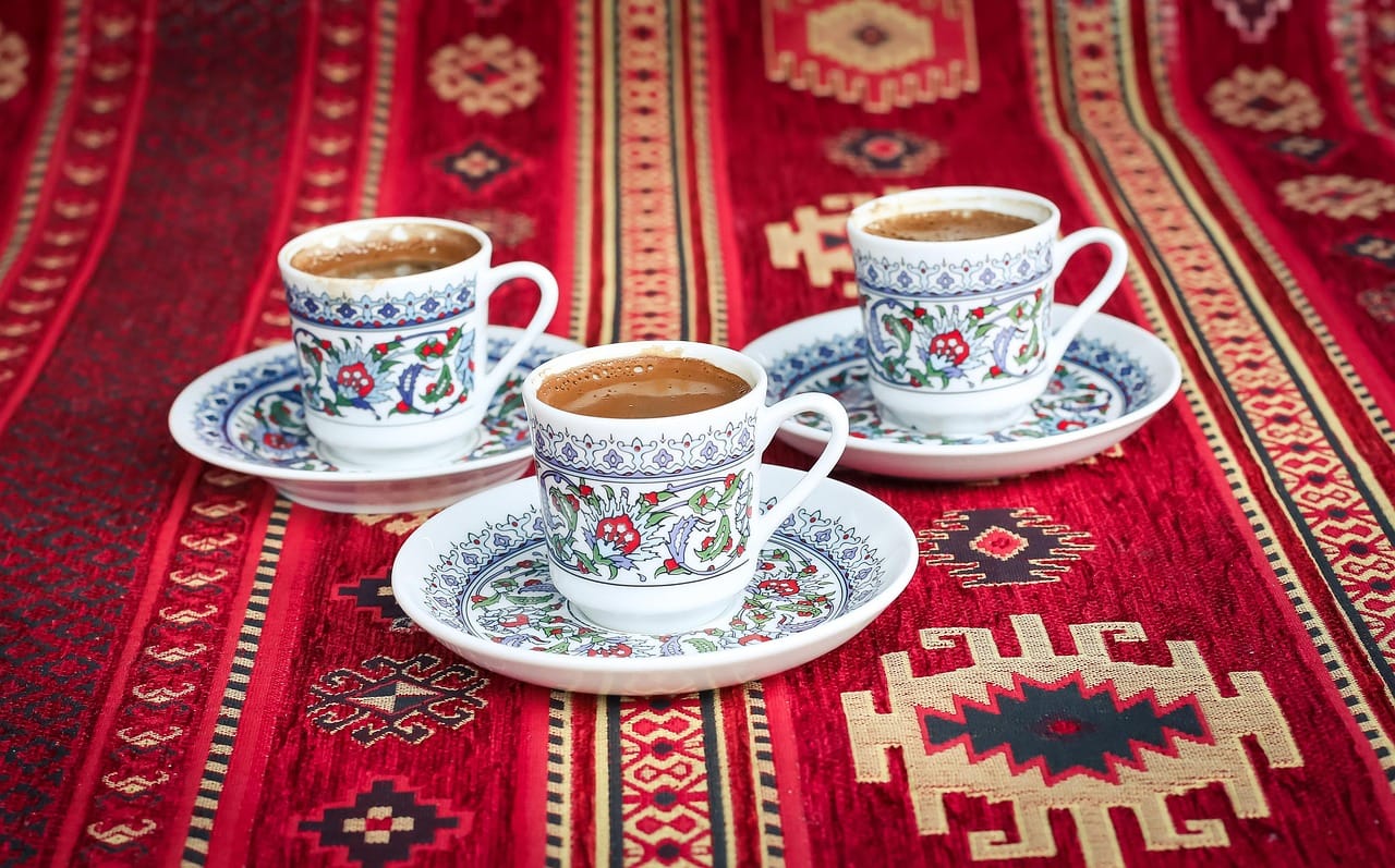 Drei verzierte Mokkatassen stehen auf einem traditionellen orientalischen Teppich.