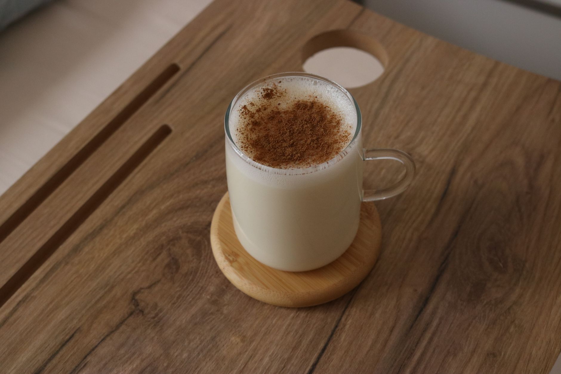 Eine Glastasse mit cremigem, heißem Salep und Zimtpulver auf einem Holzuntersetzer.