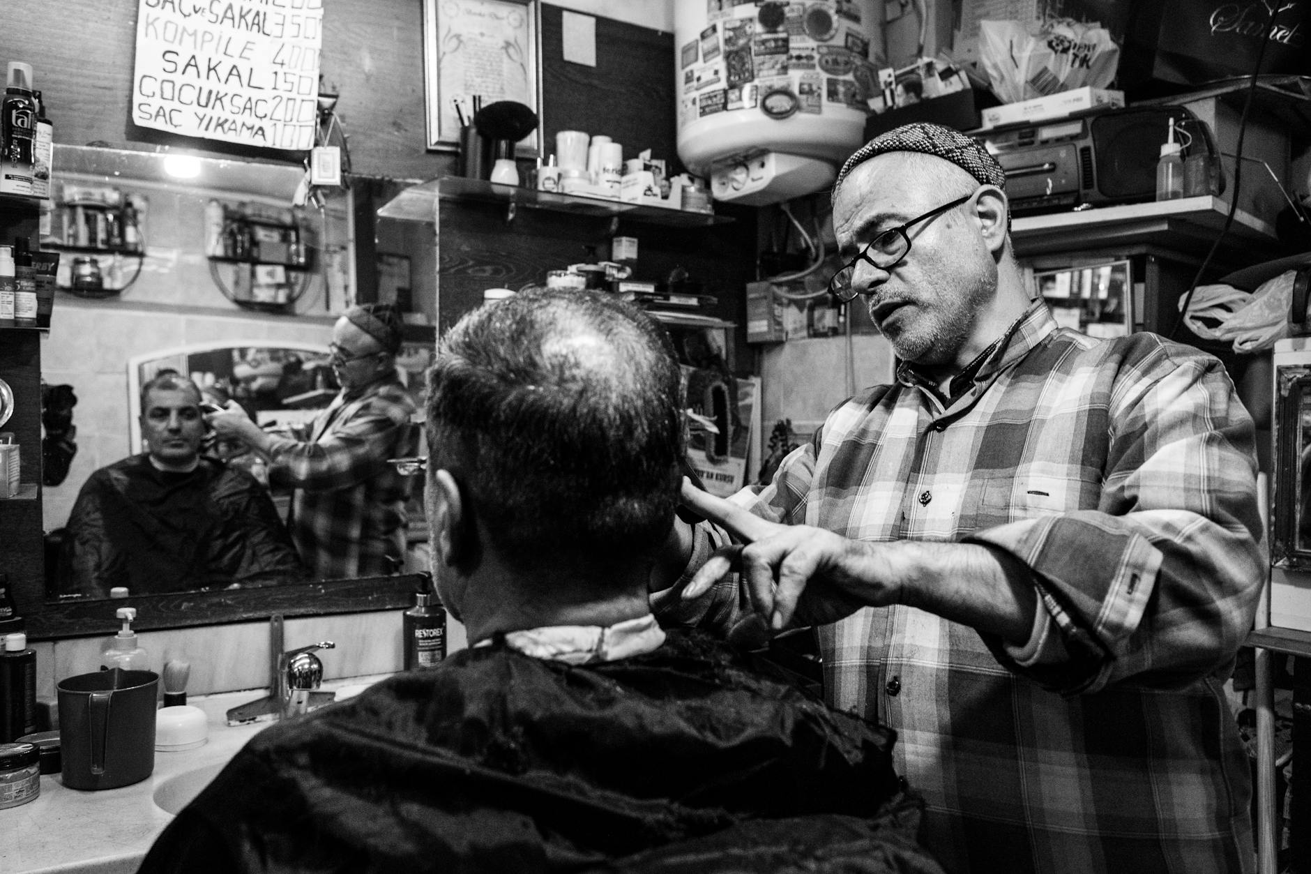 Ein Barbier in Istanbul schneidet Haare vor einer Tafel mit türkischen Preisen.