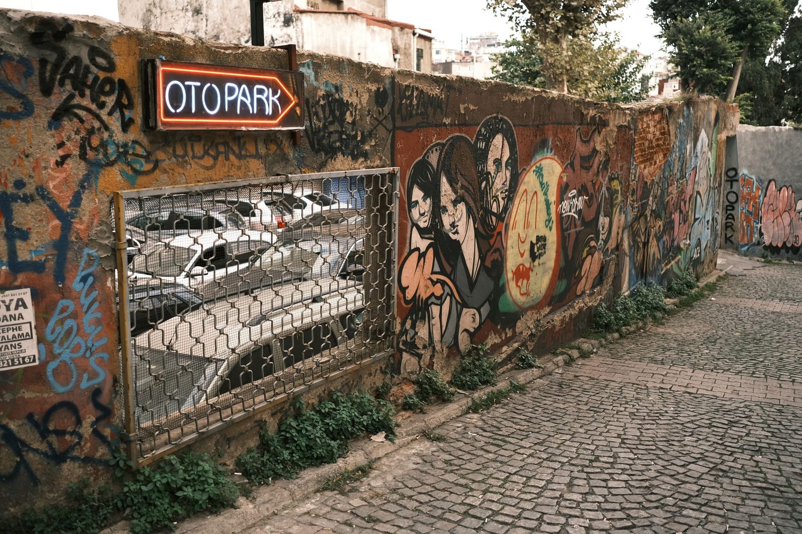 Farbige Wandbilder und Graffiti schmücken eine Mauer entlang der Gasse.